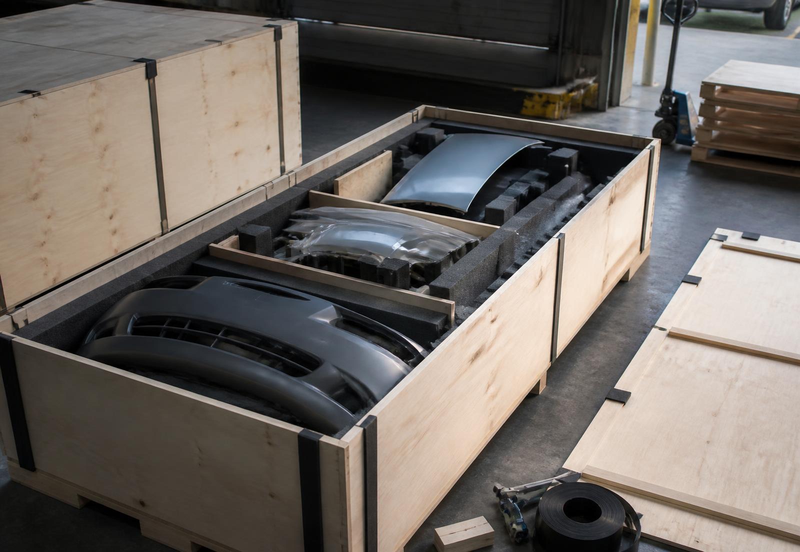 Body panels and a bumper foam-blocked inside a plywood export crate at a loading dock
