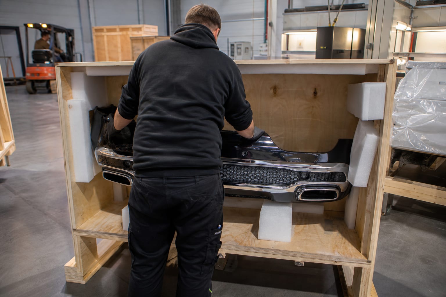 Warehouse technician foam-blocking a Mercedes body panel into a plywood export crate