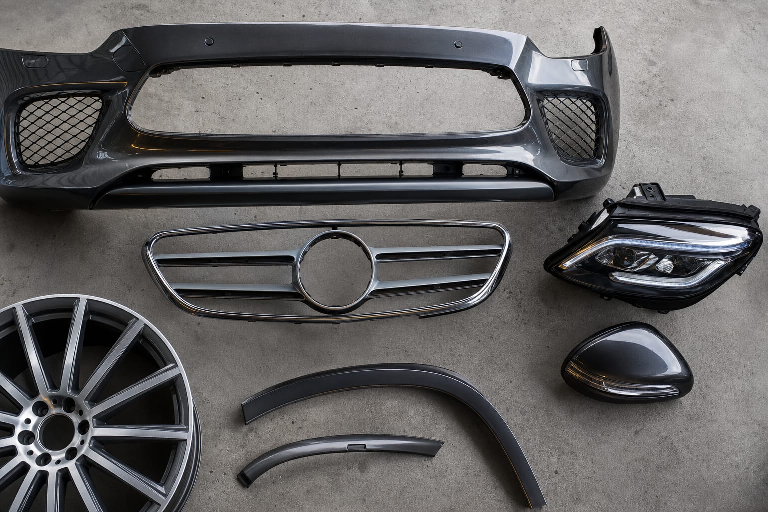 Mercedes-Benz bumper, grille, headlight, mirror cap and forged wheel laid out on an inspection table